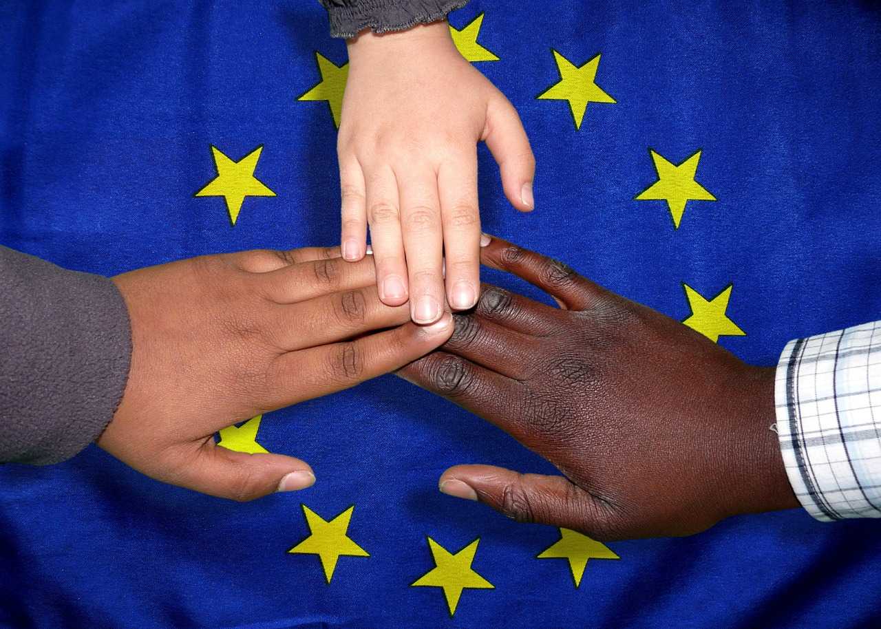 mani di 3 bambini di diversa etnia sopra la bandiera europea